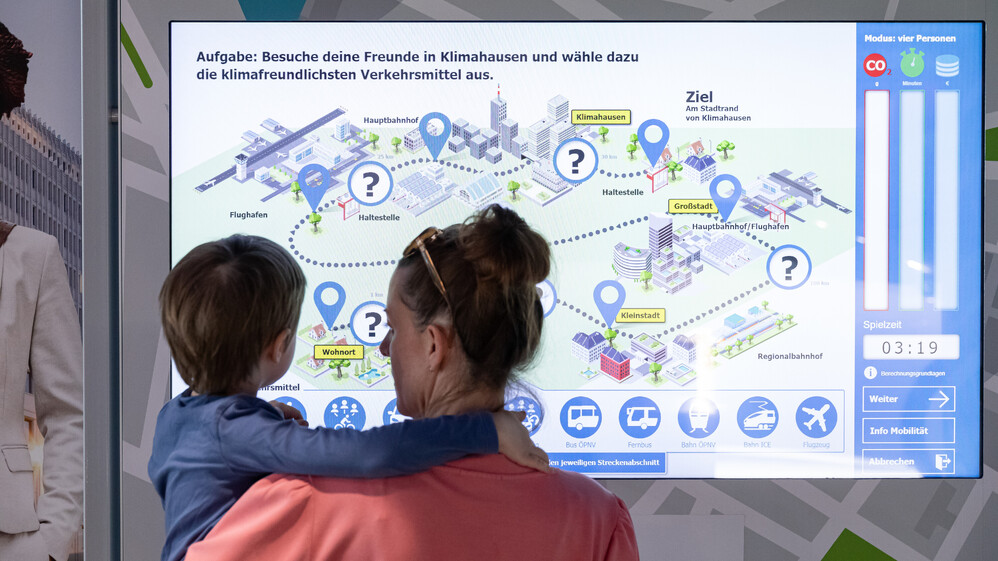 Mutter mit Sohn auf dem Arm vor dem Bildschirm des Mobilit&auml;tsspiels.